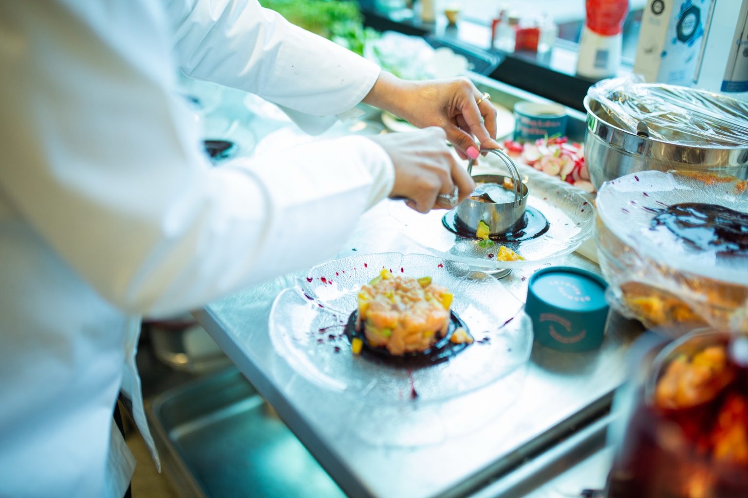 Sakirat Waraich plating a dish in a white chef coat, focused, composing the plate.
