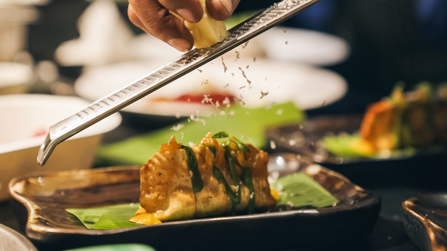 A carefully plated Nila dish with vibrant colours and sauce details, hand grating finishing element on top.