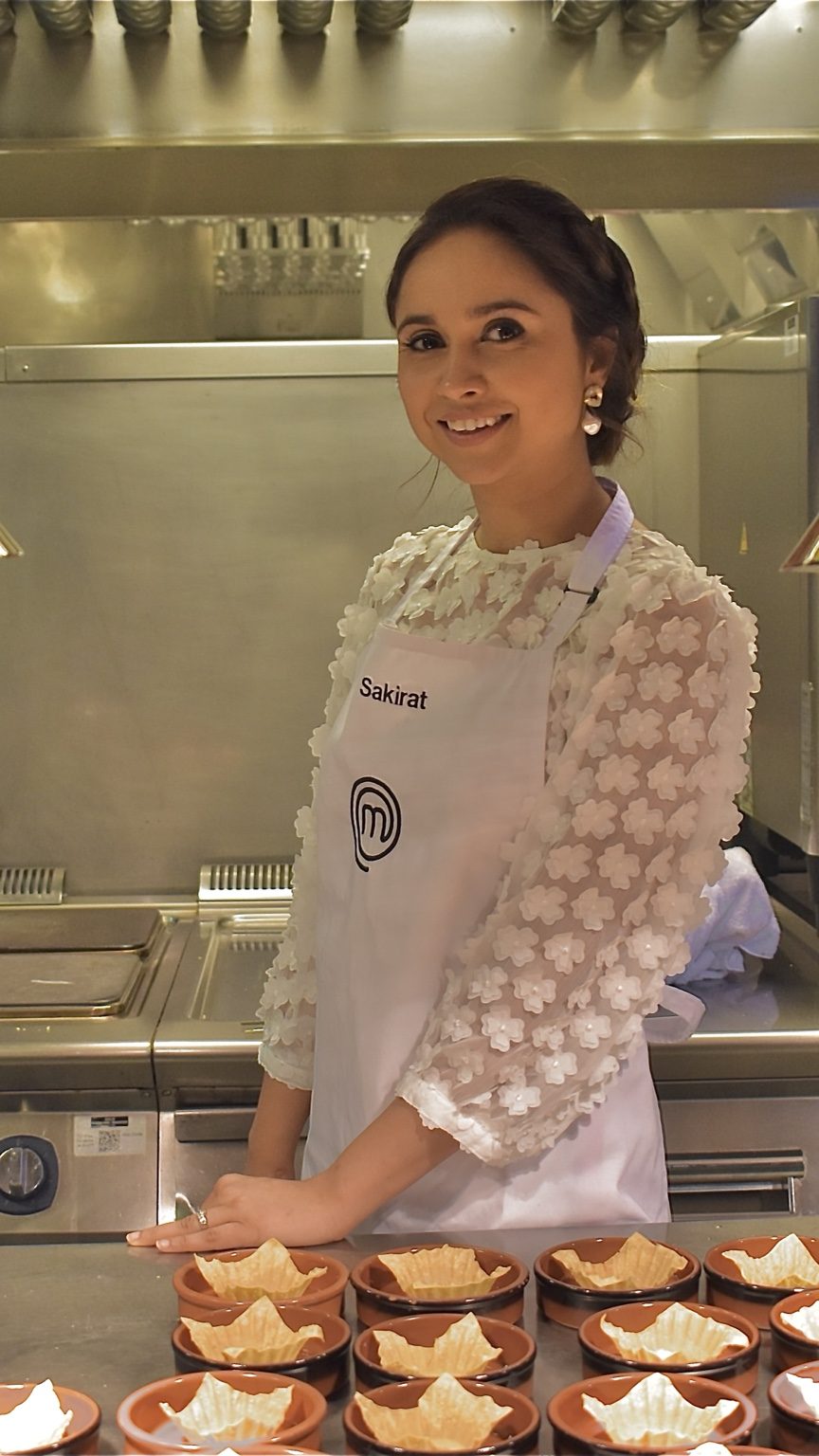 Sakirat Waraich in a MasterChef apron preparing food in a professional kitchen.