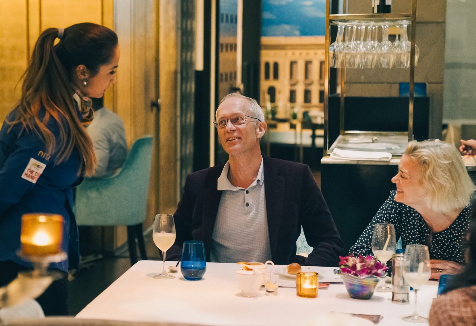 Sakirat Waraich speaking with guests during a dining experience at an upscale restaurant.